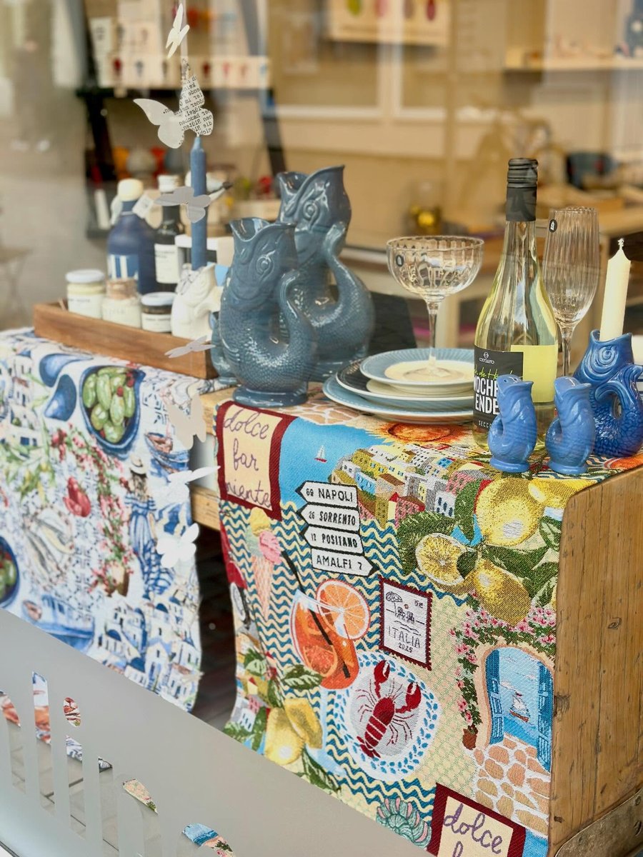Dekoriertes Schaufenster mit blauen Fischkruegen, Tischwaesche mit Italien-Motiven, Weinflasche, Sektschale und Kerzen