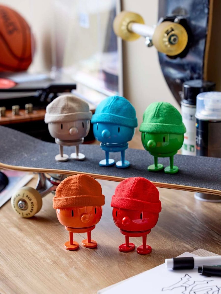 Fuenf Hoptimist-Figuren Hipster mit gestrickten Muetzen in Beige, Blau, Gruen, Orange und Rot auf einem Skateboard